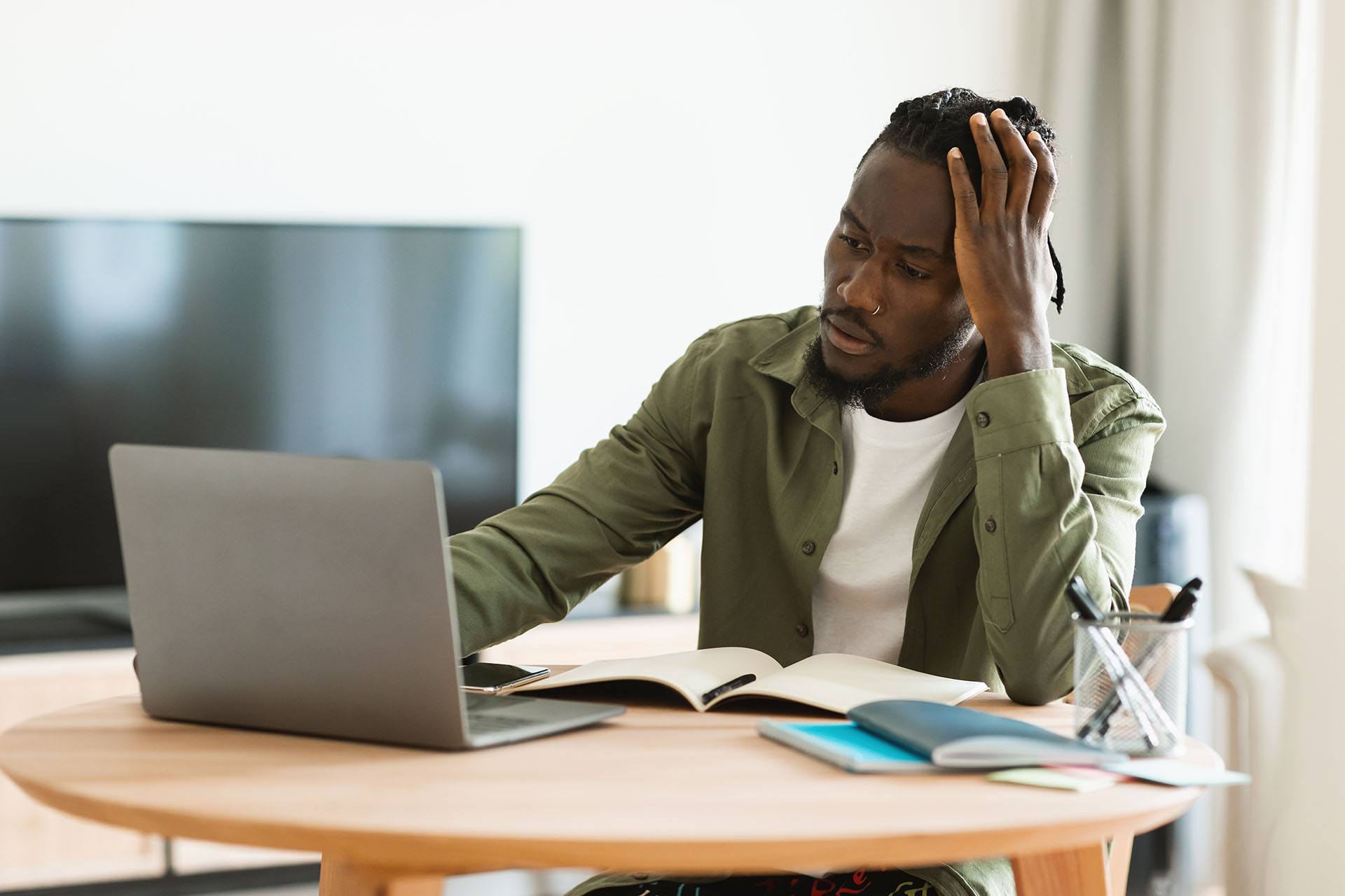 Thoughtful black man using laptop computer working online and thinking about business, touching head, sitting at home office. Entrepreneurship issues concept